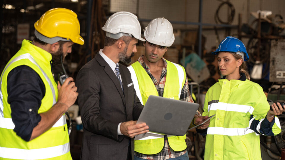 A group of people in hardhats gathering around a laptop.