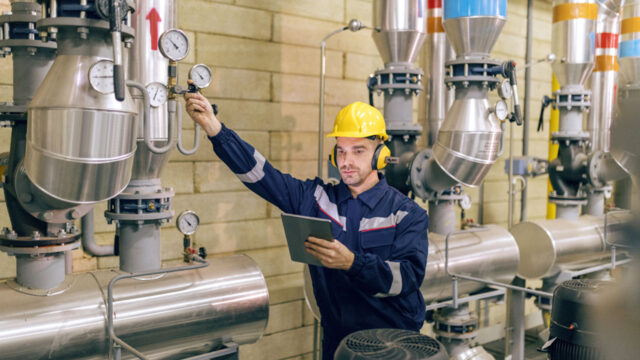 A photograph of a man in a hard hat and ear protection checking a machine.
