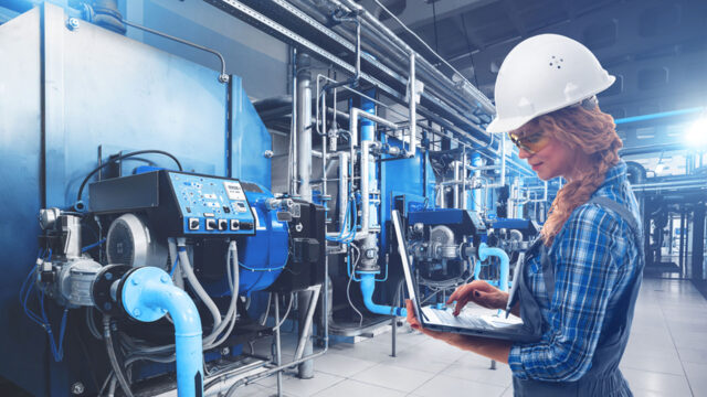 A woman in a hardhat holding a laptop.