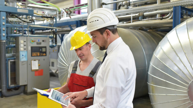 A photograph of two people in hard hats looking at a tablet.