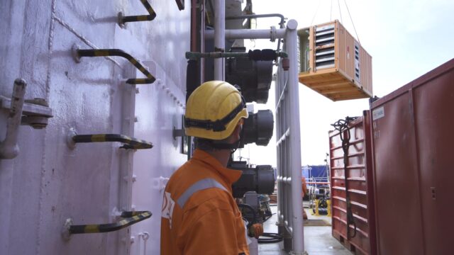 A photograph of a man in a hardhat on a oil rig.