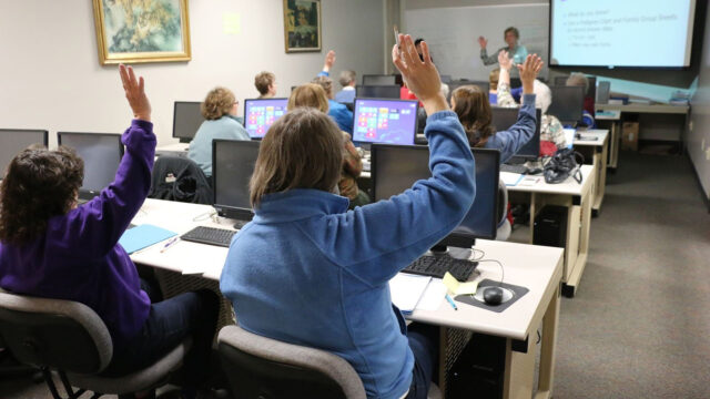 A group of people in a training class holding their hands up..