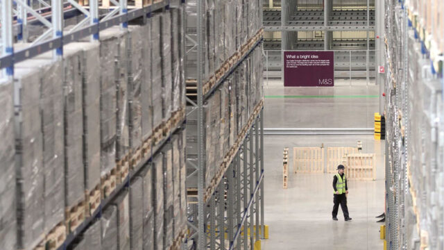 A photograph of a large warehouse with a worked in a high-vis jacket.