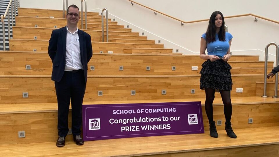 Tim and Ashleigh standing next to a School of Computer Prize Winners sign.